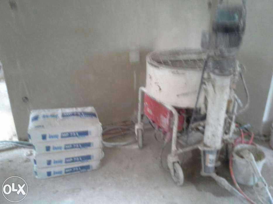 Agregat tynkarski obok stosu worków z zaprawą MP 75 L, przygotowany do prac wykończeniowych na budowie. Widoczne przewody i wiadro.