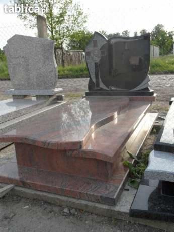 Nagrobek z czerwonego granitu z falistym wykończeniem blatu, na tle innych pomników i zieleni, w dziennym świetle.