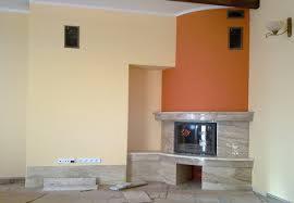 Wykończony kominek z marmurową obudową, pomalowany na pomarańczowo fragment ściany. Widoczne gniazdka elektryczne i fragment sufitu z drewnianą belką.