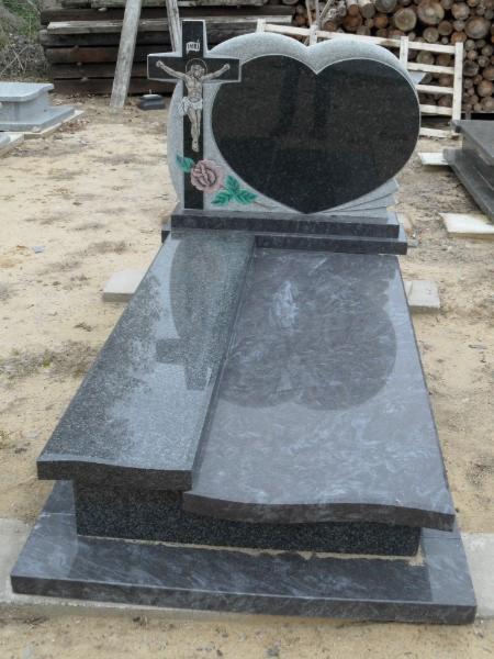 Granitowy nagrobek z krzyżem i sercem, zdobiony różą, na tle składowanych desek. Kamienna konstrukcja z polerowanego granitu w odcieniach szarości i czerni.