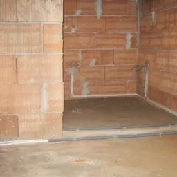 Surowy stan wnętrza z widocznymi przewodami elektrycznymi i instalacją w ścianach z cegły dziurawki.