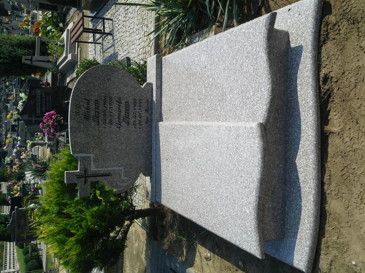 Jasnoszary, granitowy nagrobek z wyrytym krzyżem i inskrypcjami, otoczony zielenią na cmentarzu. Ujęcie z boku, z widocznymi innymi nagrobkami w tle.