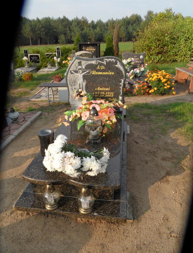 Granitowy nagrobek z kwiatami i zniczami na cmentarzu, w tle drzewa. Napis na nagrobku: S.P. Romaniec, Antoni 07.06.1932 - 01.09.2007.