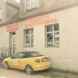 Żółty kabriolet zaparkowany przed budynkiem z napisem 'Kredyty Ubezpieczenia', okna oklejone reklamami pożyczek.