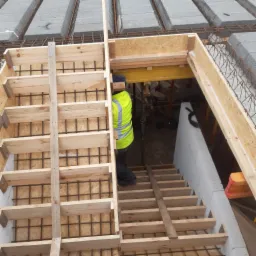 Budowa stropu Teriva: szalunek z desek i płyty OSB, widoczna stal zbrojeniowa, pracownik w kamizelce odblaskowej, bloczki betonowe stropowe