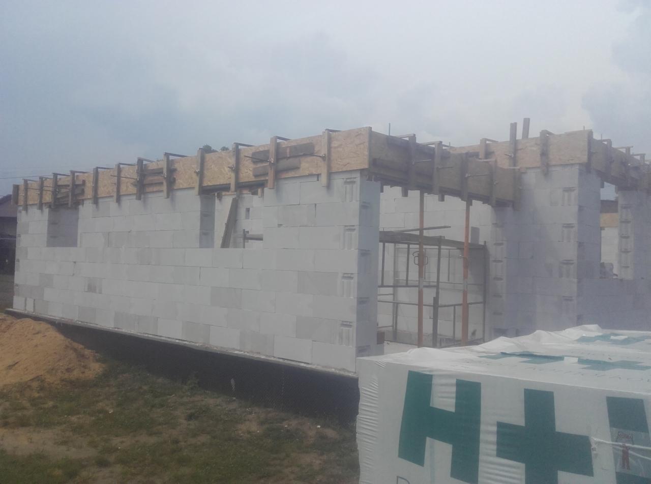 Wznoszenie ścian domu z betonu komórkowego, widoczne szalunki stropu i paleta bloczków Ytong na pierwszym planie.