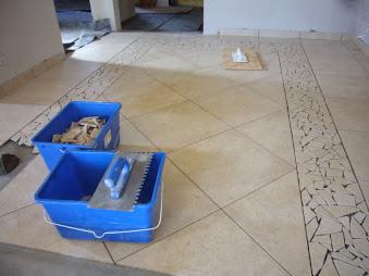 Beżowa podłoga z ułożonym wzorem mozaiki, niebieskie pojemniki z narzędziami glazurniczymi, widok z góry, jasne światło.