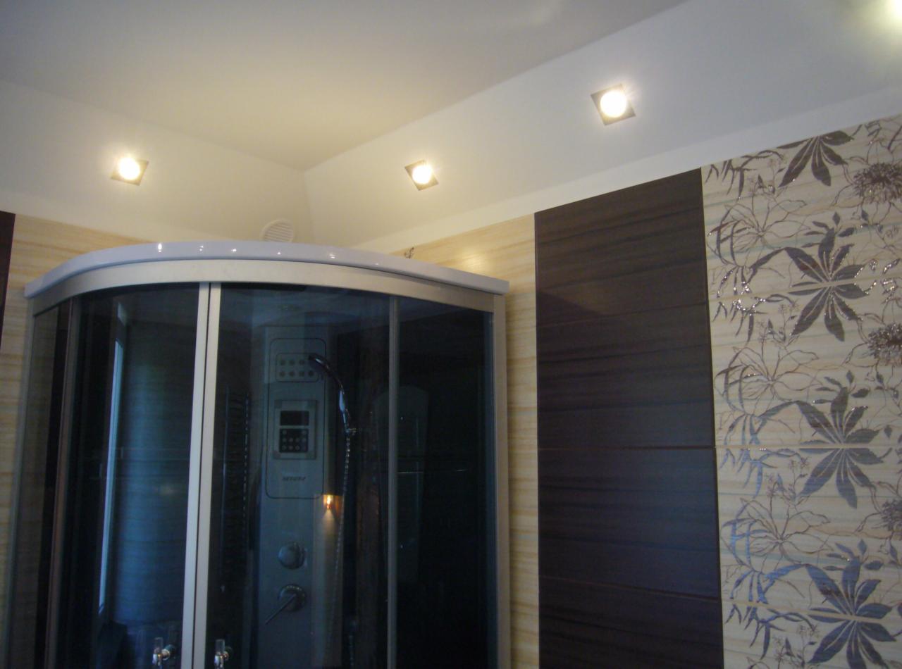 Nowoczesna kabina prysznicowa z hydromasażem, obudowana płytkami w odcieniach beżu i brązu, oświetlenie punktowe w suficie. Estetyczne wykończenie.