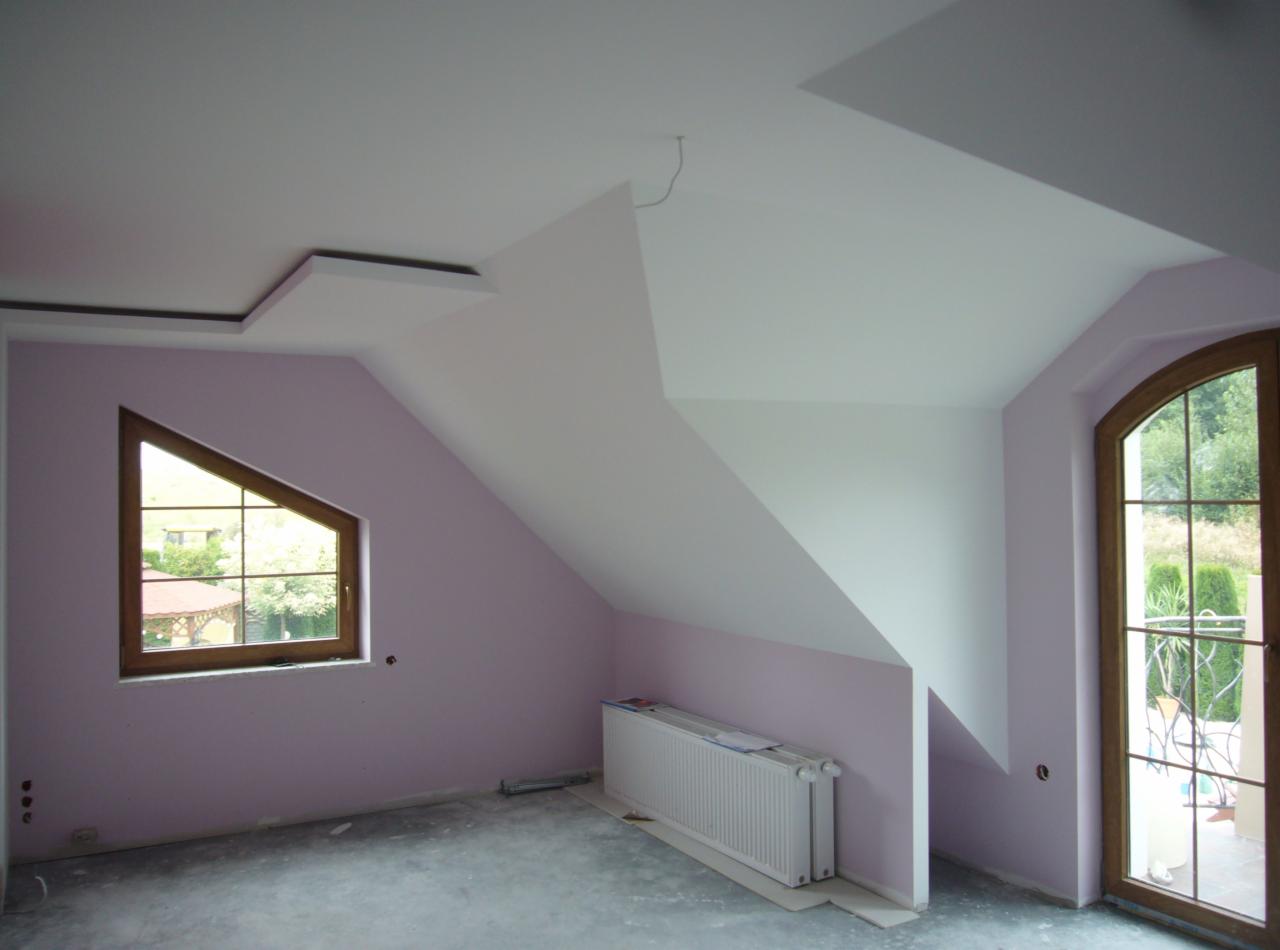 Pokój na poddaszu z oknem trójkątnym i drzwiami balkonowymi. Ściany pomalowane na liliowo, sufit biały z nietypową geometrią. Grzejnik pod ścianą, surowa podłoga.