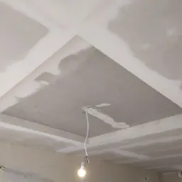 Sufit podwieszany z płyt gipsowo-kartonowych w trakcie szpachlowania, widoczna żarówka na kablu i fragment drabiny.
