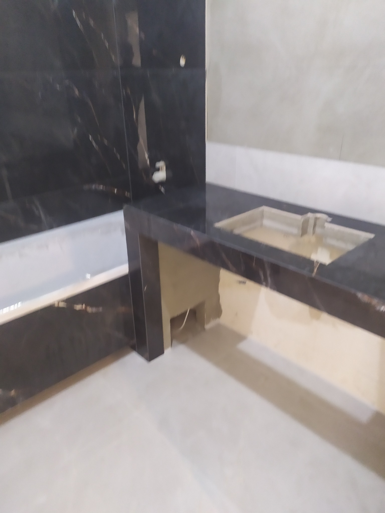 Łazienka w trakcie wykańczania: wanna obłożona czarnym marmurem, umywalka wpuszczana w blat z czarnego marmuru, ściany częściowo wykończone, widoczne niedokończone podłączenia.