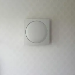 Szary, kwadratowy panel wentylacyjny z okrągłym wlotem, zamontowany na ścianie z delikatnym wzorem w jasnych odcieniach szarości.