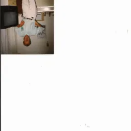 Obrócone o 180 stopni zdjęcie wnętrza kuchni z mężczyzną w jasnych spodniach i koszuli. Widoczny telewizor, szafki i kalendarz na ścianie.