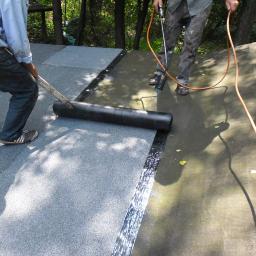 Malowanie Dachów Sławomir Jankowski - Dekarze podczas uszczelniania dachu papą termozgrzewalną przy użyciu palnika i wałka. Widoczne fragmenty dachu pokryte papą i narzędzia pracy.