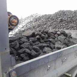 Przyczepa wypełniona węglem kamiennym, w tle hałda węgla z fragmentami śniegu.