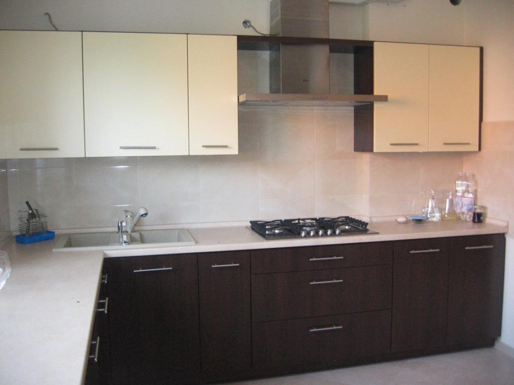 Nowoczesna kuchnia z górnymi szafkami w kolorze kremowym i dolnymi w odcieniach brązu, z blatem w jasnym beżu i płytą gazową, oświetlona przez srebrny okap.