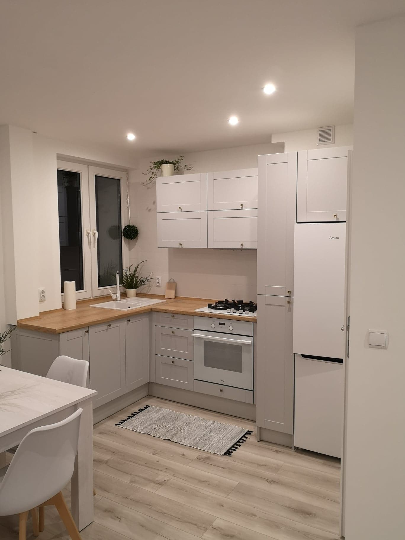 Jasna, nowocześnie urządzona kuchnia w Świerklańcu z drewnianym blatem, szarymi szafkami, białym sprzętem AGD i ozdobnymi roślinami.