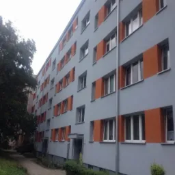 Odnowiony blok mieszkalny we Wrocławiu, szara elewacja z pomarańczowymi akcentami wokół okien, widok z poziomu chodnika.