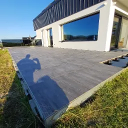 Nowoczesny taras z szarych płyt na regulowanych wspornikach, z widokiem na góry i dom. Czyste linie i minimalistyczny design.