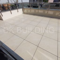 DK BUILDING - Jasne, kwadratowe płytki na balkonie z metalową balustradą i donicami. Widok z góry, delikatne oświetlenie.