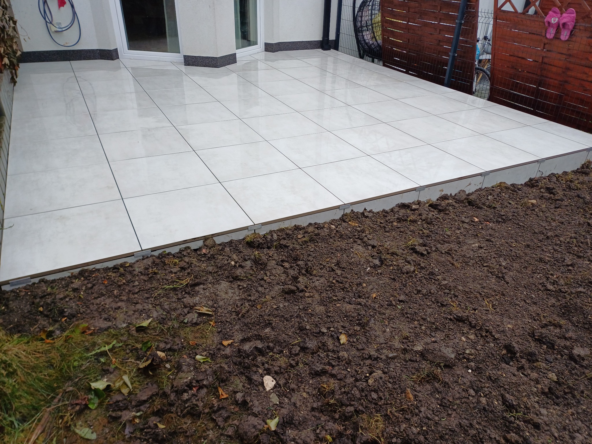 Jasny taras z płytek ceramicznych, widok z poziomu gruntu. Uwagę zwraca precyzyjne ułożenie płytek i estetyczne wykończenie krawędzi tarasu.