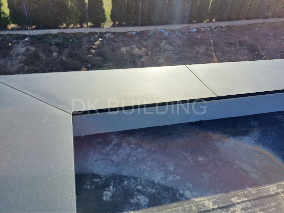 Szary, metalowy obrys balkonu z widokiem na zieleń w tle. Wykończenie z blachy, detale łączeń. Widoczny fragment powierzchni balkonu.