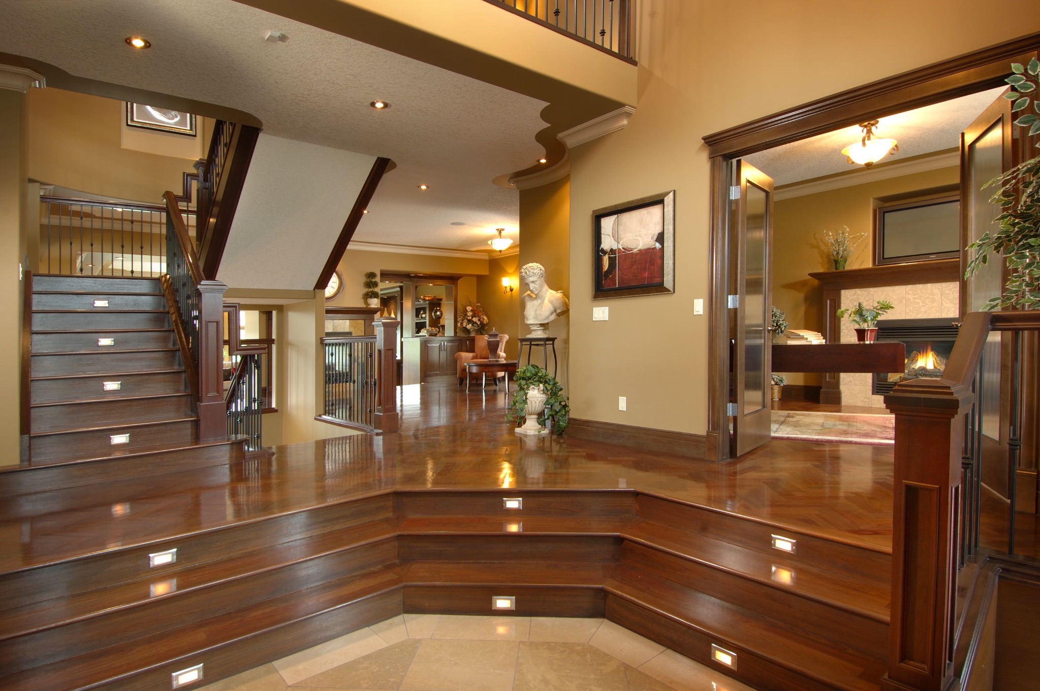 Eleganckie wnętrze domu z drewnianymi schodami z podświetleniem, parkietem i widokiem na salon z kominkiem. Klasyczny wystrój z elementami dekoracyjnymi.