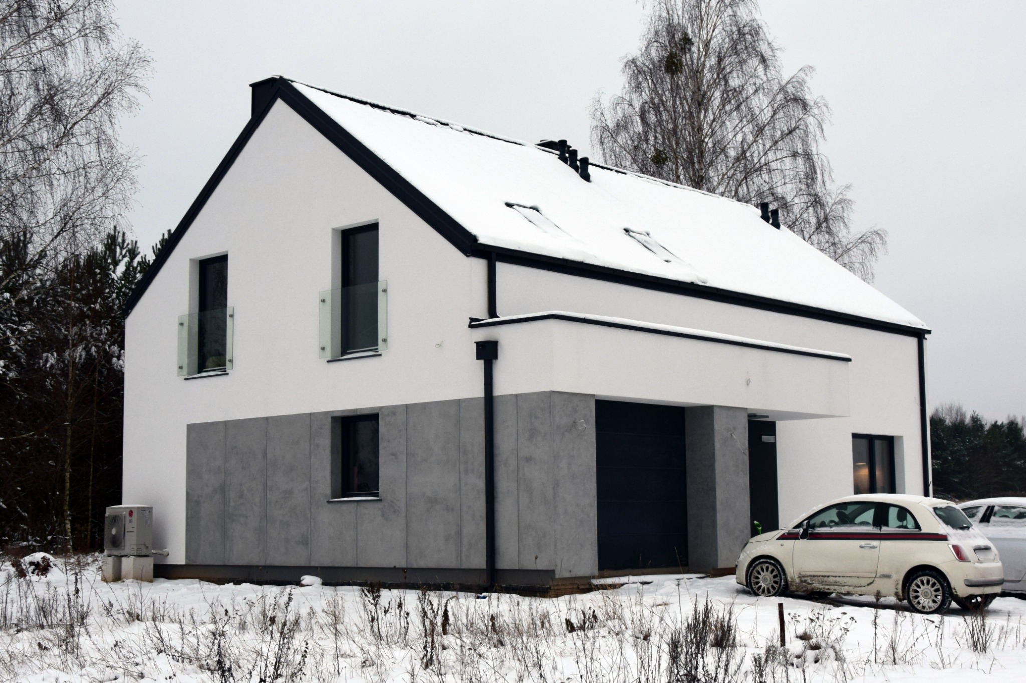 Nowoczesny, dwukondygnacyjny dom z płaskim dachem pokrytym śniegiem, białą fasadą z szarymi panelami na dole i czarnymi obramowaniami okien, garażem w bryle budynku oraz białym Fiatem 500...