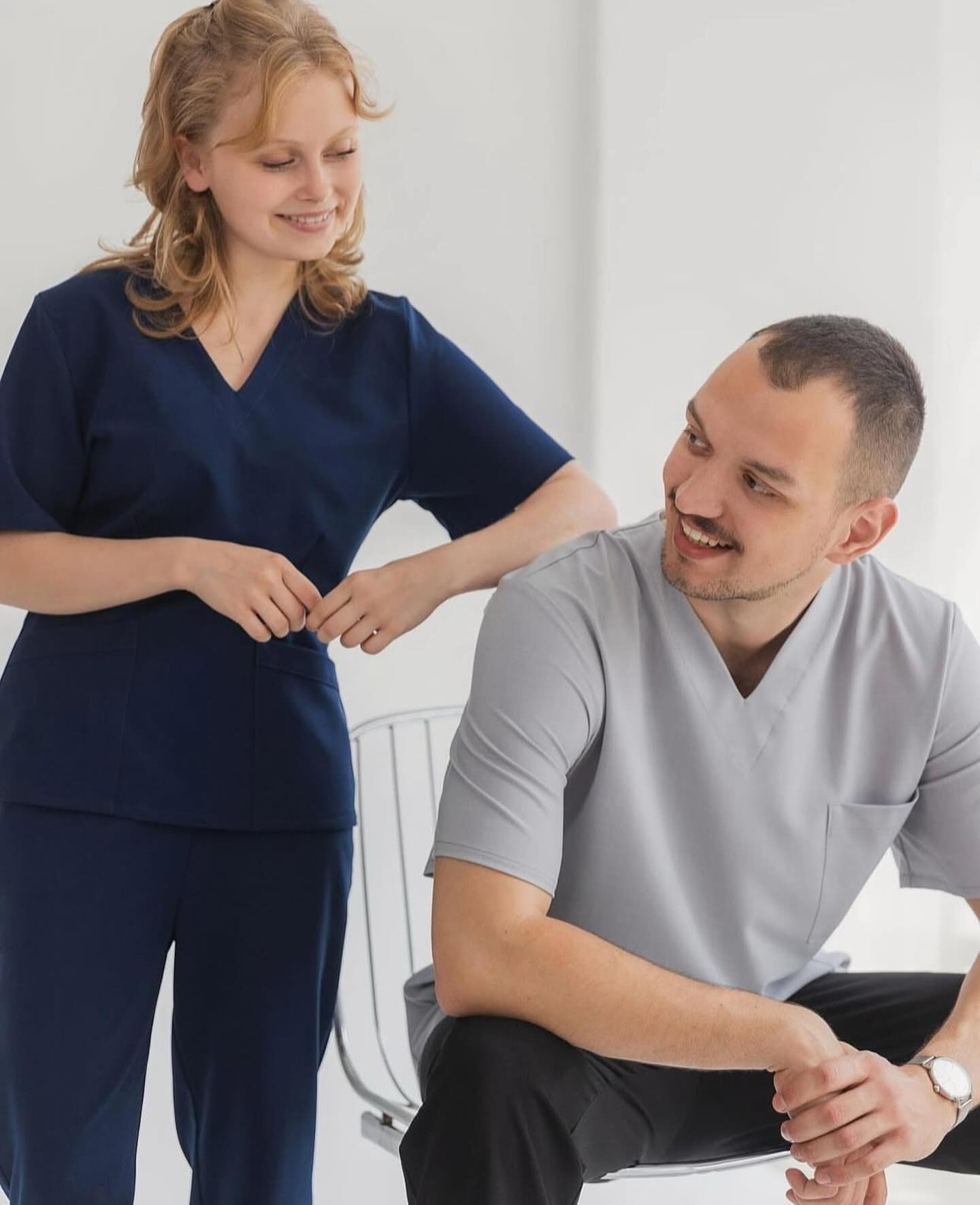 Dwoje uśmiechniętych modeli prezentuje odzież roboczą: granatowy komplet damski i szary męski, oboje w strojach z krótkim rękawem i dekoltem w serek.