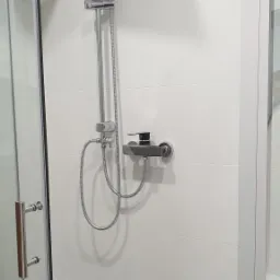 Nowoczesna kabina prysznicowa z chromowaną armaturą i deszczownicą, białe płytki na ścianie, minimalistyczny design.