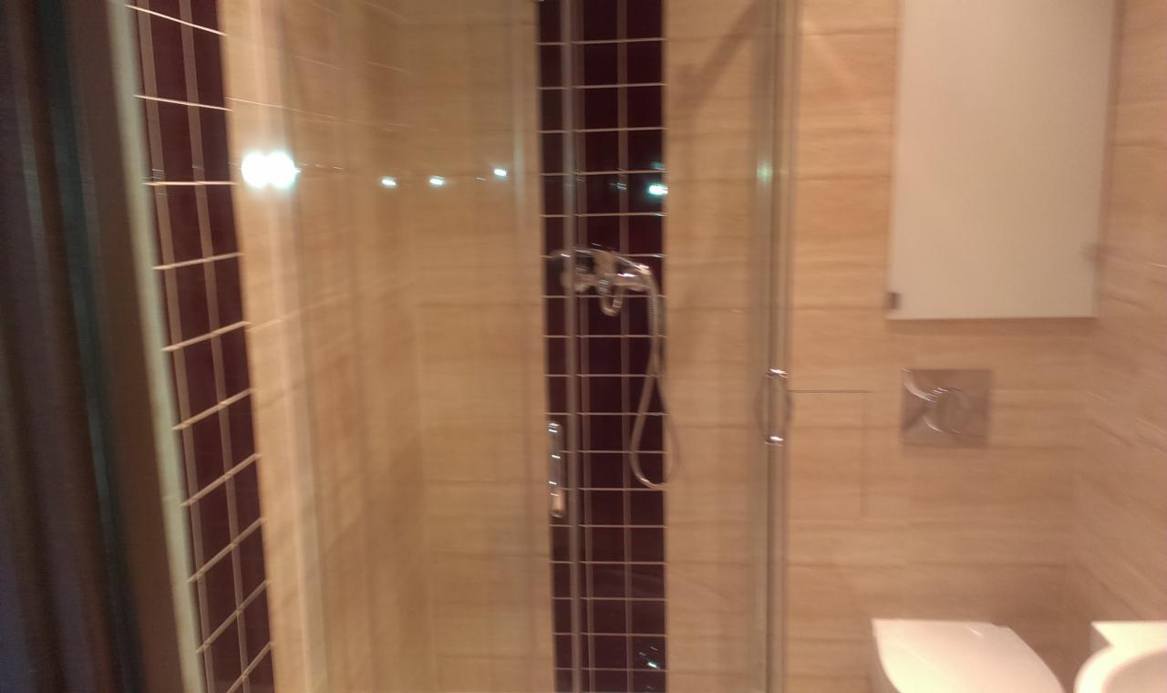 Wykończona kabina prysznicowa z brązowymi akcentami płytek, umywalką i toaletą. Widoczne detale wykończenia i armatura.