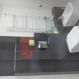 Wyremontowana łazienka z czarnymi płytkami, białą toaletą i bidetem. Na ścianie biały grzejnik. Czerwony akcent na ścianie dodaje charakteru.