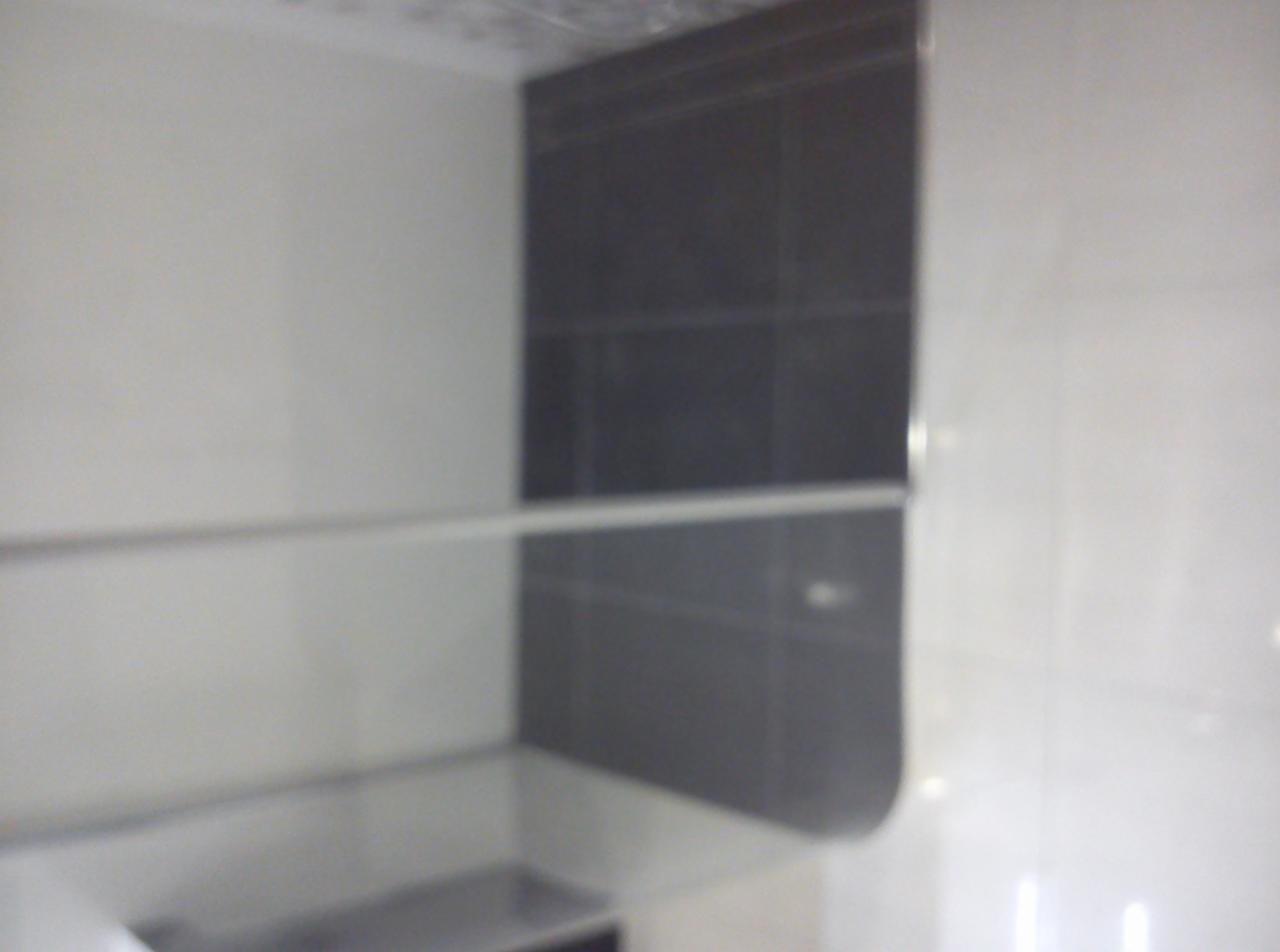 Częściowy widok ściany łazienki z szarymi i białymi płytkami, oddzielonymi poziomą listwą. Widoczne odbicie światła na powierzchni płytek.