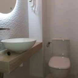 Nowoczesna łazienka z okrągłym lustrem, umywalką nablatową na drewnianym blacie i wiszącym sedesem z białą ceramiką.