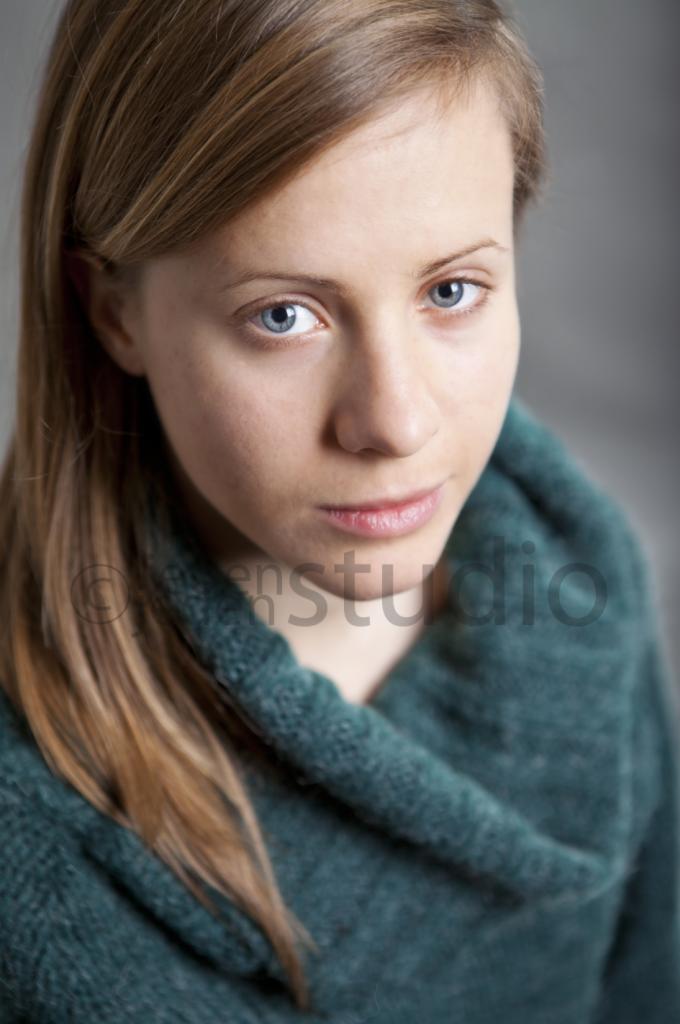 Portret kobiety z jasnymi włosami i niebieskimi oczami, ubrana w zielony sweter. Ujęcie z góry, stonowana kolorystyka, widoczny znak wodny.