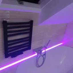 Łazienka na poddaszu z wanną, chromowaną baterią i czarnym grzejnikiem drabinkowym, oświetlona fioletowym światłem LED.