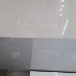 Połączenie jasnych i ciemnych płytek ceramicznych na ścianie, widoczny fragment toalety, minimalistyczny styl.