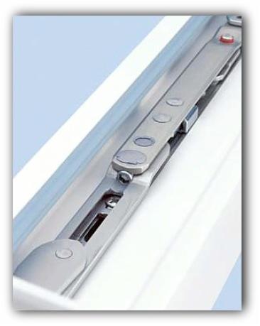 Detal prezentujący mechanizm otwierania okna z widocznym metalowym ramieniem i elementami mocującymi, osadzony w białej ramie okiennej.