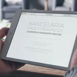 Osoba trzyma tablet prezentujący stronę internetową kancelarii radcy prawnego Agnieszki Romanów-Małysa. Widoczny adres i dane kontaktowe.
