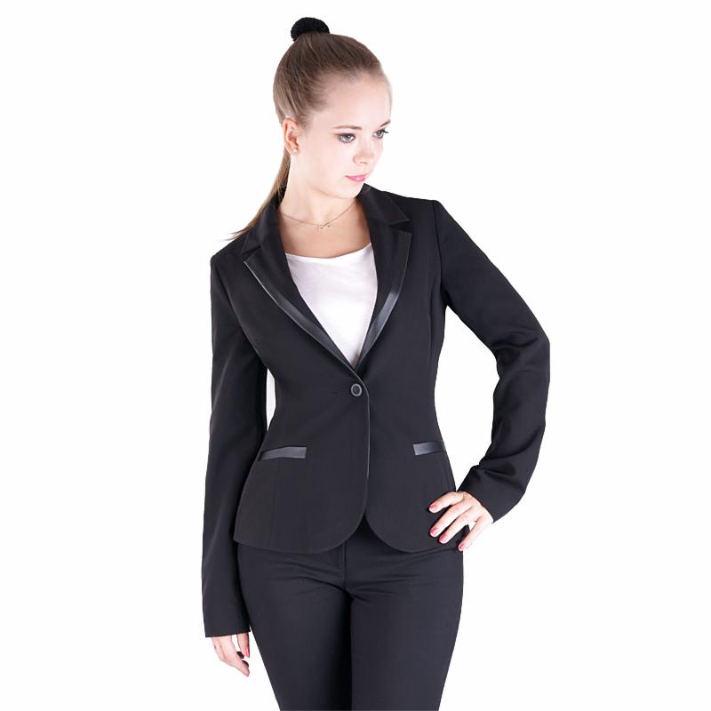 Kobieta pozuje w czarnym, dopasowanym żakiecie z satynowymi klapami i mankietami, do kompletu czarne spodnie, biała bluzka, dłoń na biodrze, włosy upięte w kok na czubku głowy.