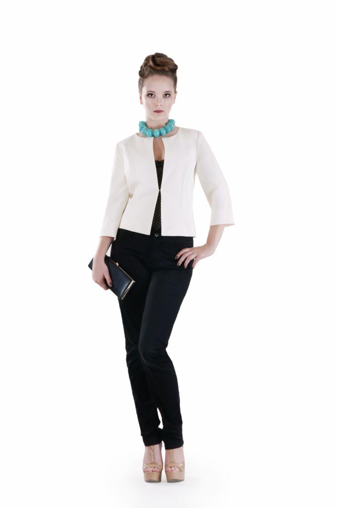 Kobieta w białym żakiecie z rękawami 3/4, czarnych spodniach i platformach, trzymająca czarną kopertówkę, z turkusowym naszyjnikiem.