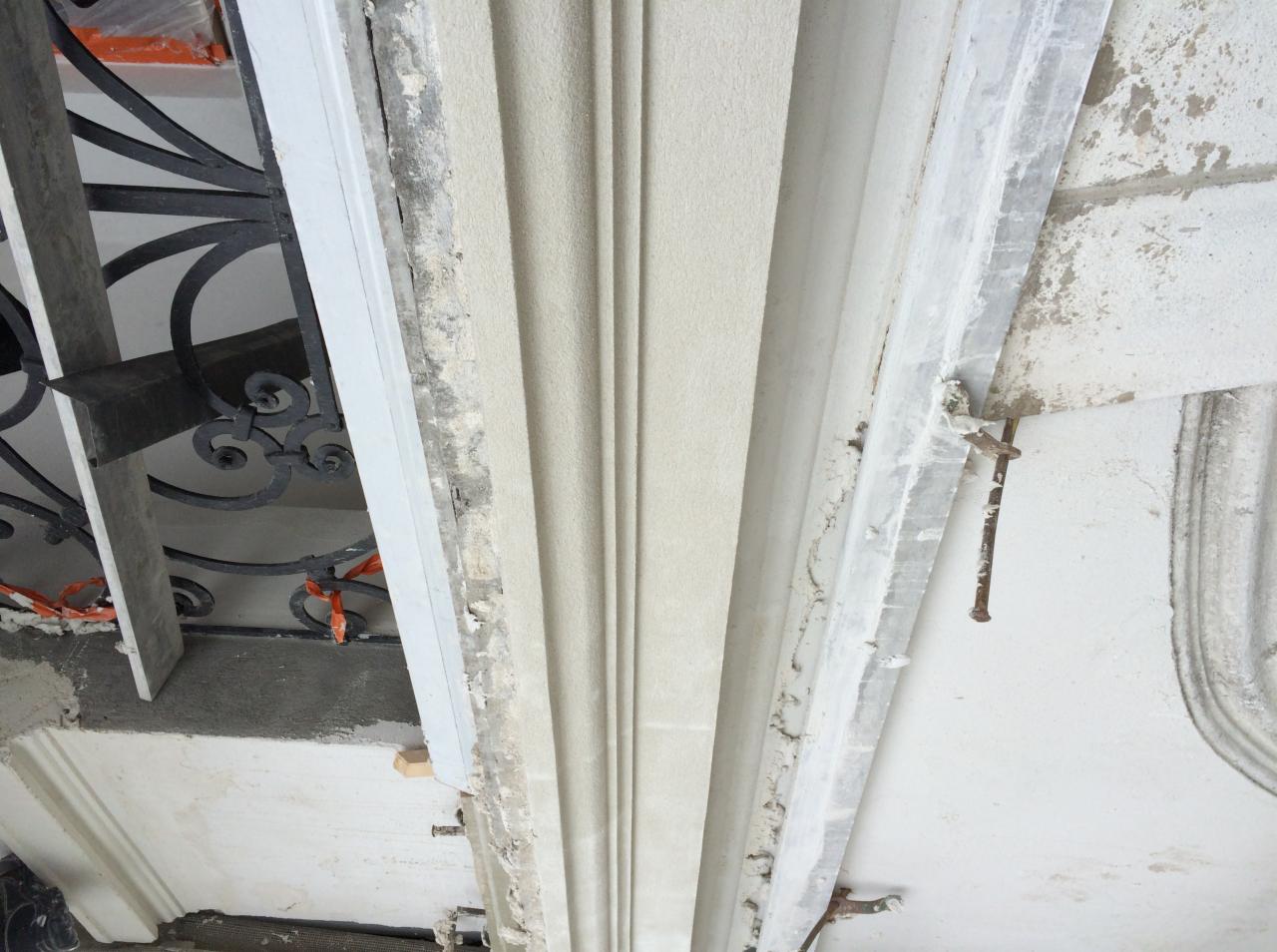 Szpachlowana ściana z dekoracyjnymi listwami podczas remontu, widoczne niedoskonałości i elementy mocujące.
