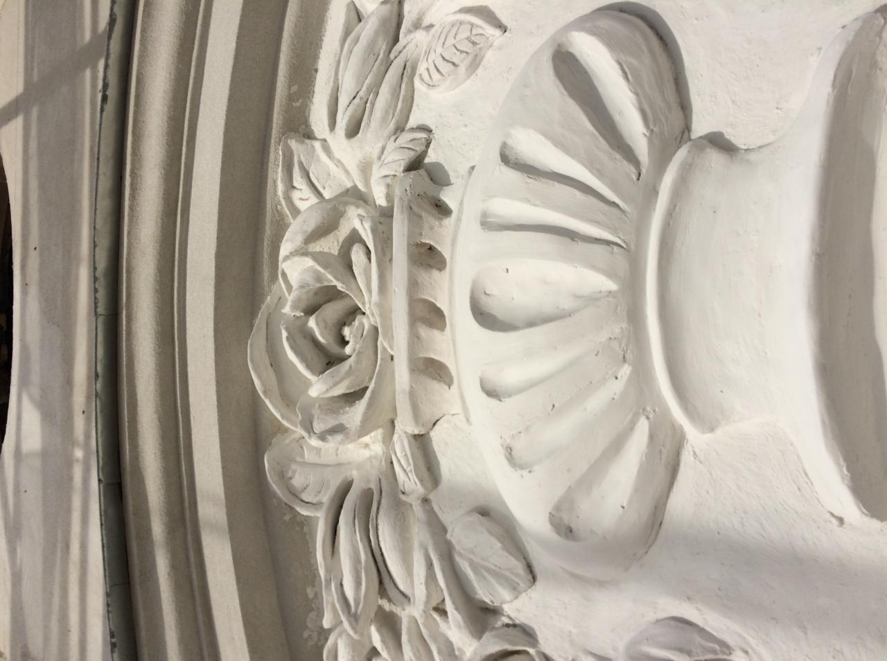 Detal dekoracyjny ściany z motywem róży, liści i wazy, wykończony białą farbą, widoczne nierówności powierzchni.