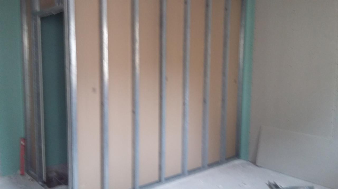 Montaż płyty karton-gips na metalowym stelażu w nowym pomieszczeniu. Widoczne profile i fragment surowej płyty. Prace wykończeniowe w trakcie.