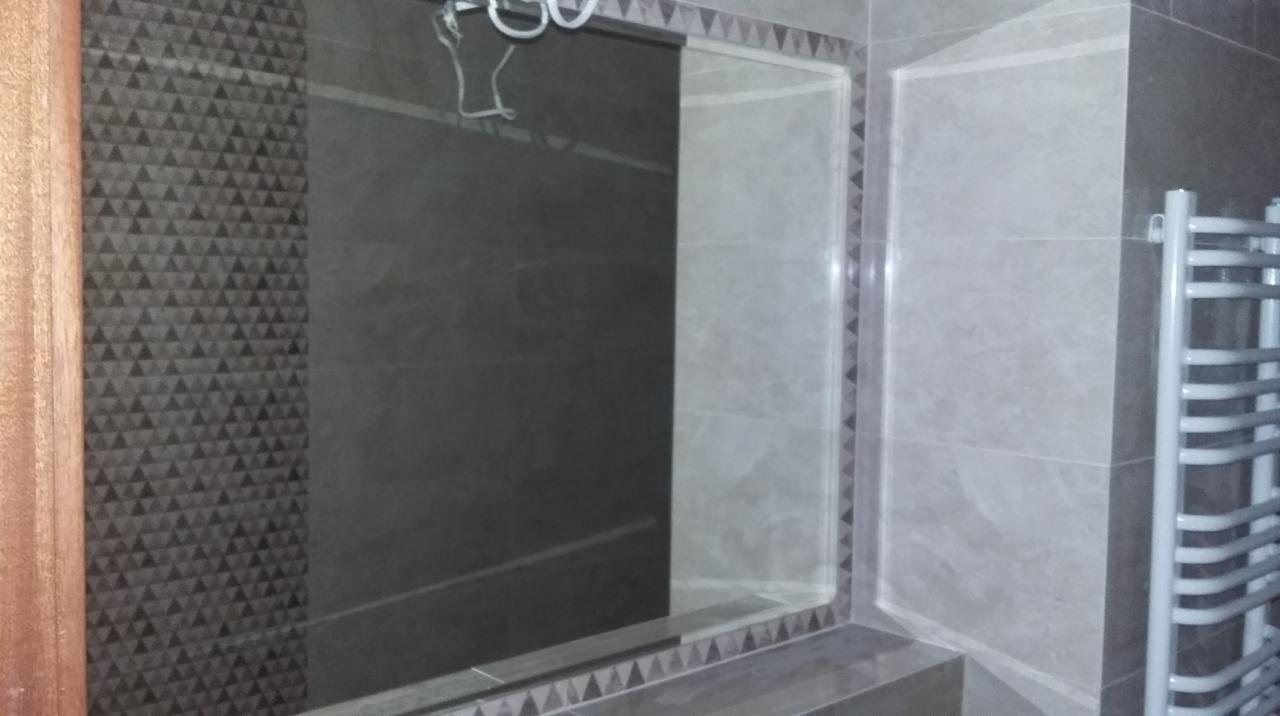 Wykończona łazienka z szarymi płytkami, dekoracyjnym wzorem trójkątów i grzejnikiem drabinkowym. Widoczne detale wykończenia i oświetlenie.