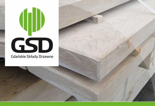 Stos jasnych desek tarcicy budowlanej z widocznym logo firmy GSD Gdańskie Składy Drzewne. Drewno ułożone warstwami, widoczne słoje i struktura drewna.
