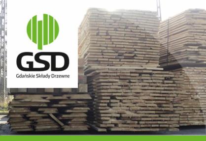 Stosy tarcicy budowlanej na placu składu drewna GSD Gdańskie Składy Drzewne, widoczne logo firmy. Drewno ułożone w równe warstwy, widok z bliska.