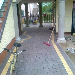 KUL-BRUK - Układanie kostki brukowej z żółtymi akcentami, widoczny rower i ubijarka w tle, prace w toku.