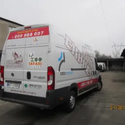 Biały bus z reklamą Taxi Express i Zoo Safari Borysew, zaparkowany na betonowym placu, widok z tyłu i boku.