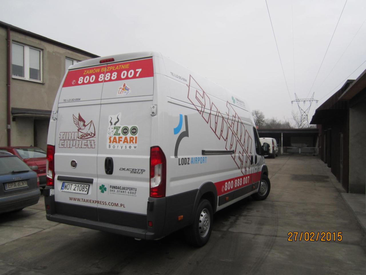 Biały bus z reklamą Taxi Express i Zoo Safari Borysew, zaparkowany na betonowym placu, widok z tyłu i boku.